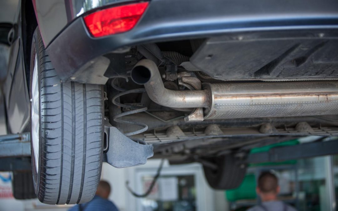 Close-up of a car's undercarriage and exhaust system while elevated on a lift in an auto repair shop during a smog check.
