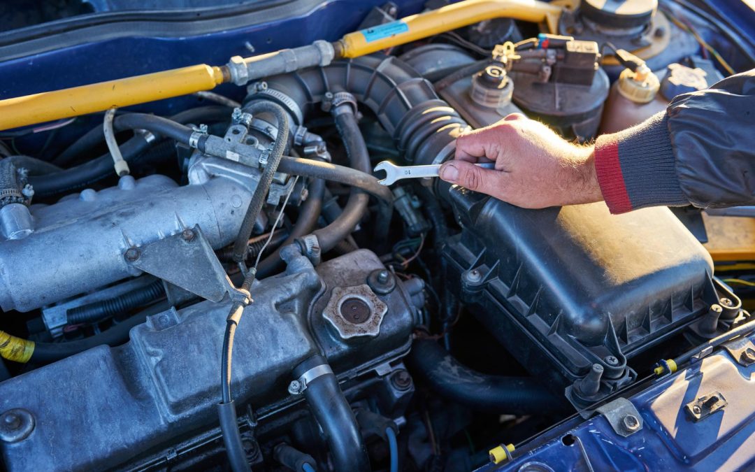 Hand holding a wrench, performing engine maintenance on a car under the hood in bright daylight.