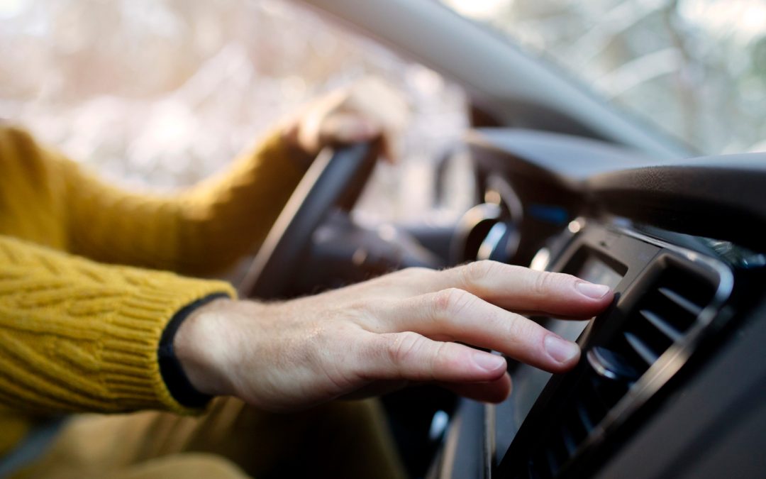 Person in a yellow sweater adjusts the dashboard controls while driving a car.
